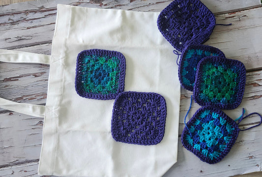 Handmade crochet granny patches in purple and teal placed on a white canvas tote bag for customization by Luniquedesigns