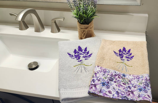 Elegant white hand towels with purple lavender embroidery folded next to a fresh lavender sprig under natural light