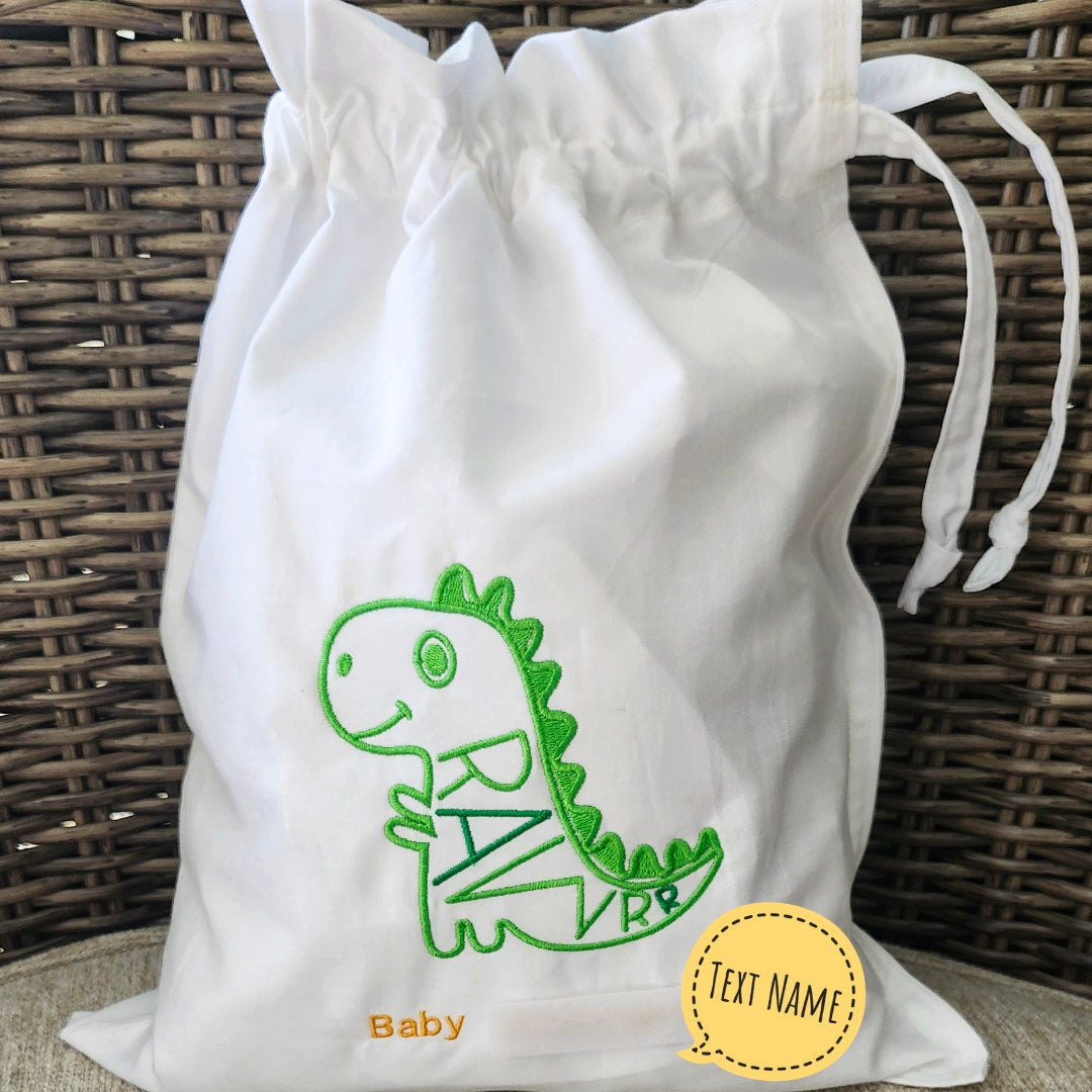 White drawstring bag with green dinosaur design and 'Baby' text on a woven surface