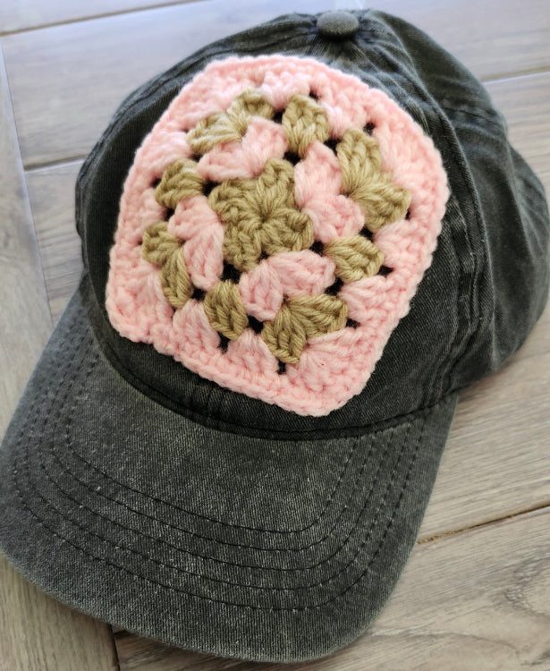 Gray cap with a pink and green crochet flower on a wooden surface