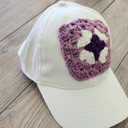 White cap with a purple and white crocheted square on a wooden surface