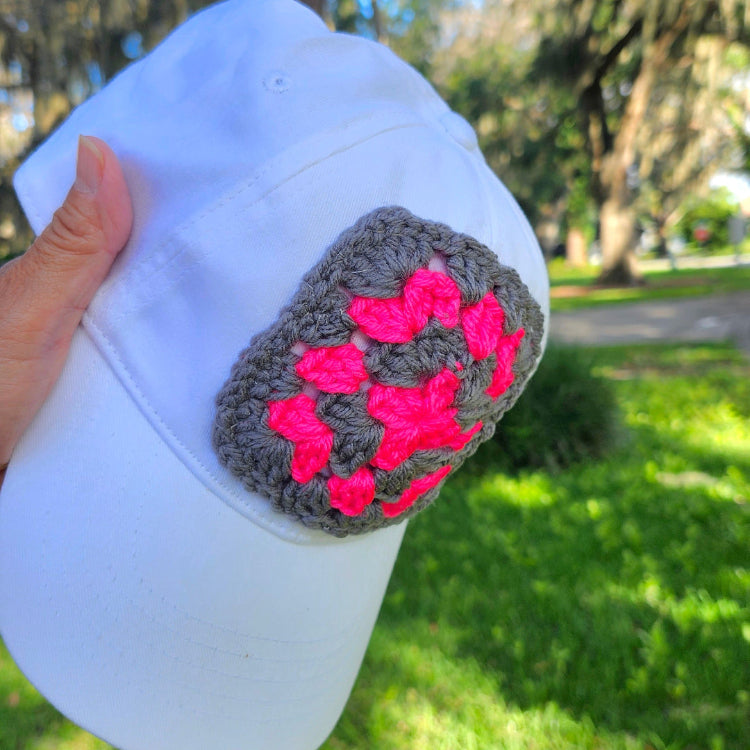 White cap with a pink and gray pattern held outdoors on grass